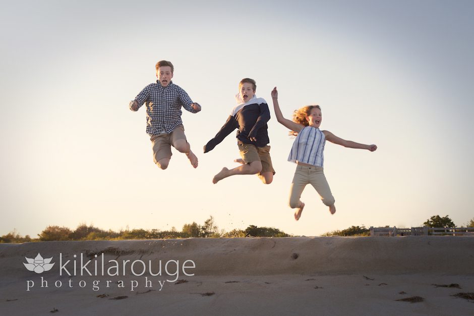 Three siblings jumping off sand dune