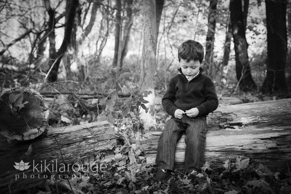 Pensive little boy sitting on log in forest