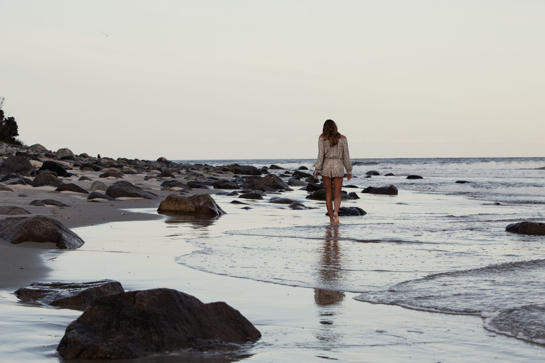 Girl walking at water's edge with rocks beach