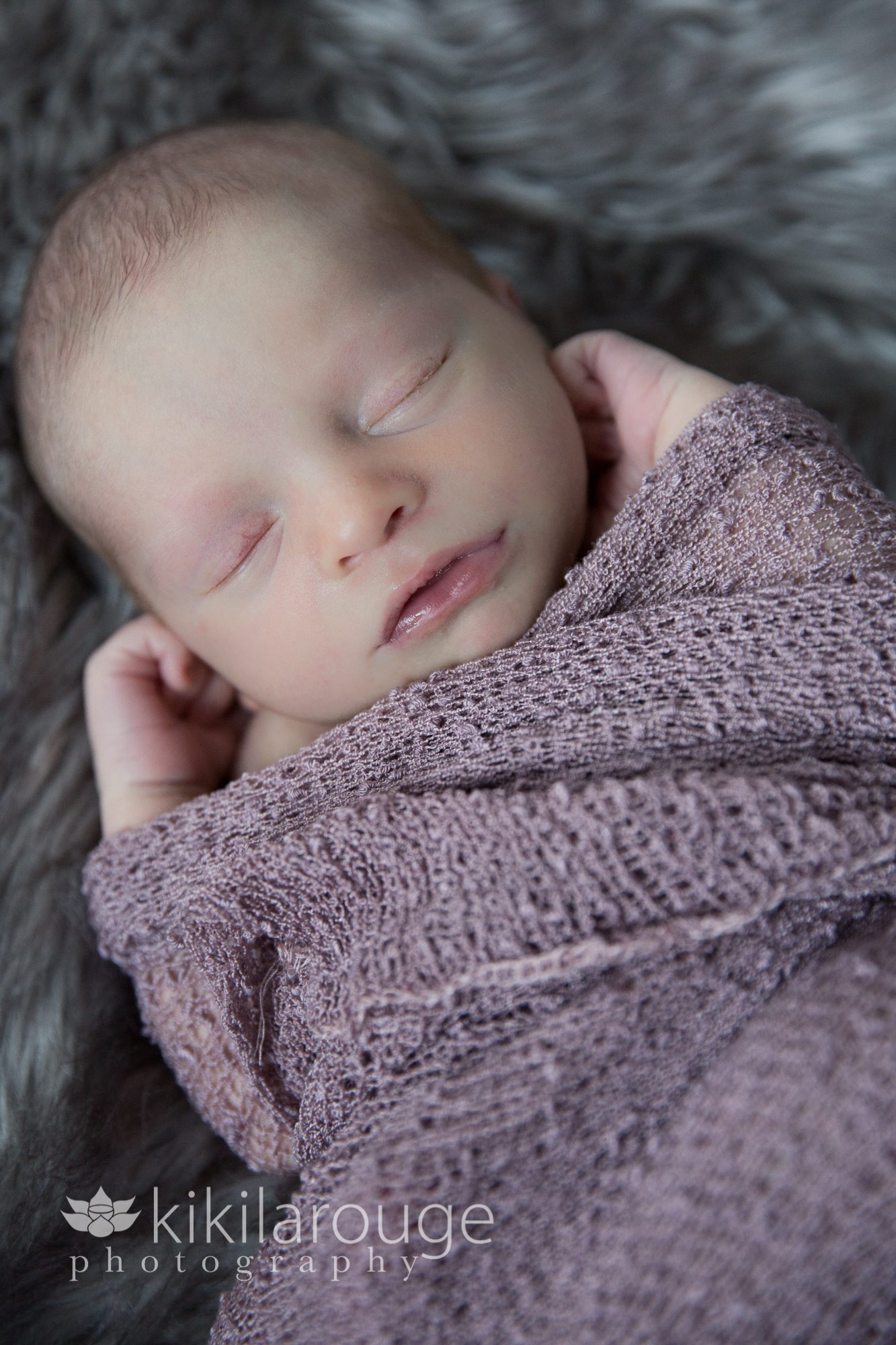 Newborn in mauve wrap on grey sheepskin