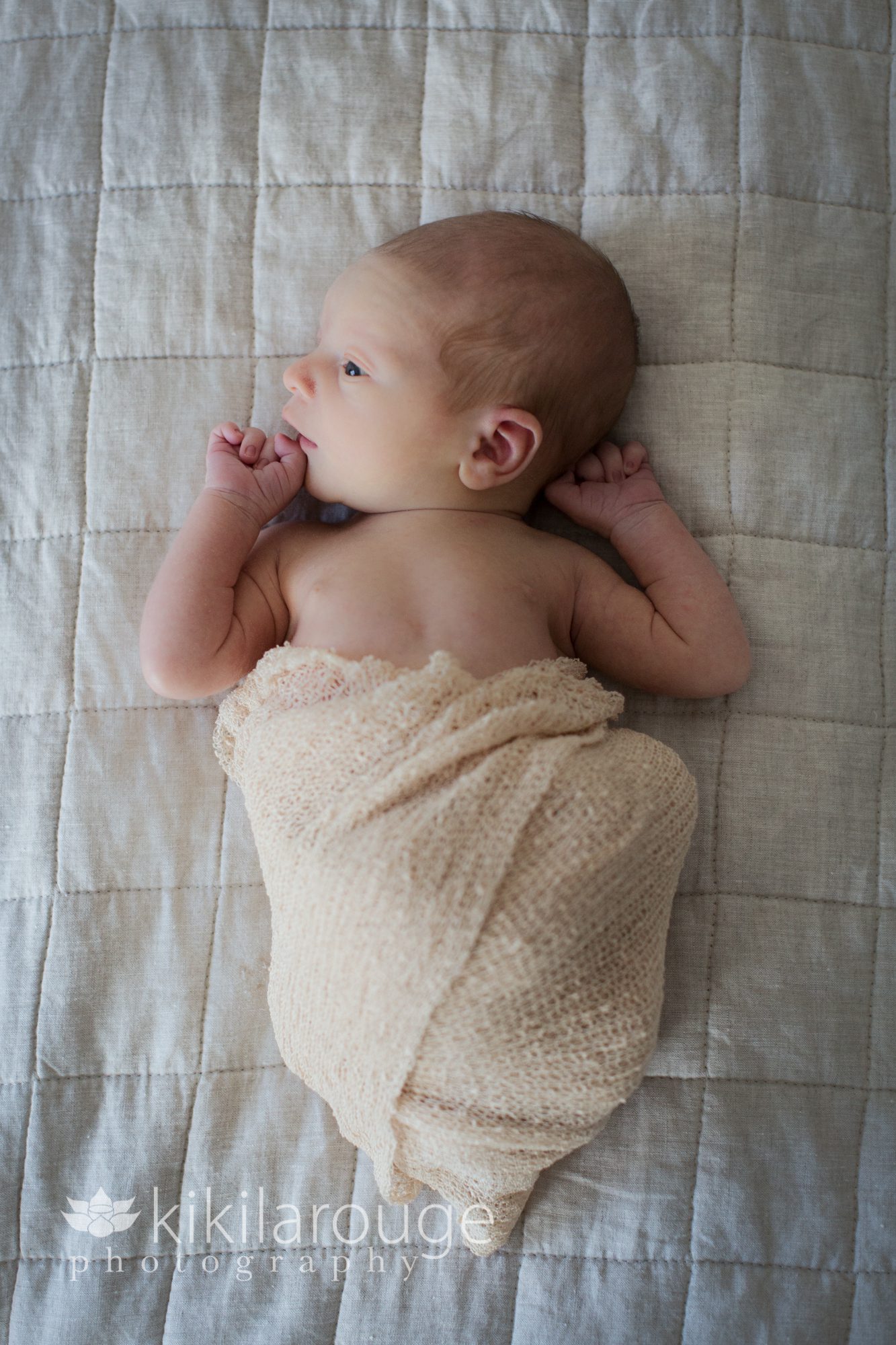 Newborn in off white wrap looking towards light