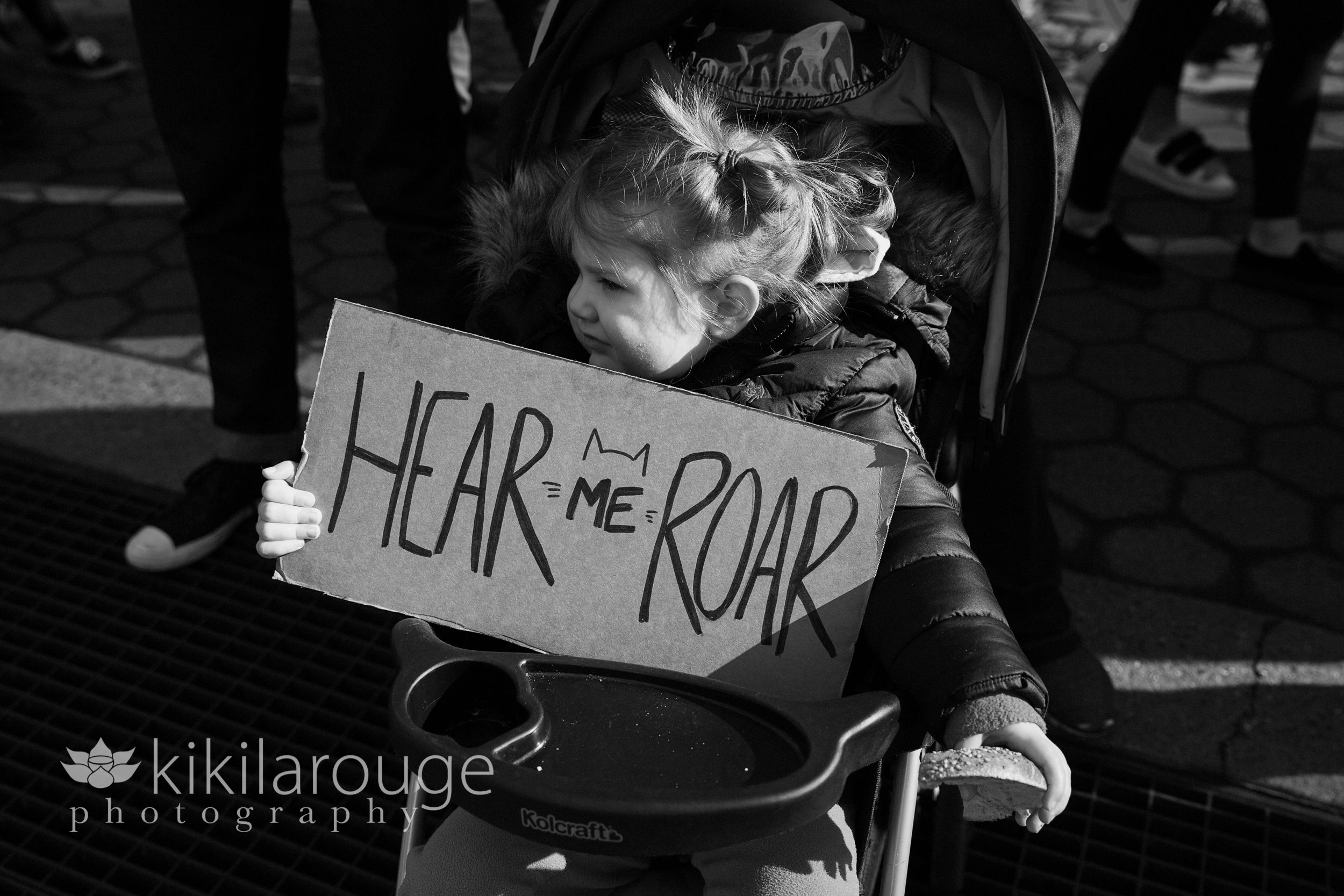 Little girl in stroller with Hear Me Roar sign