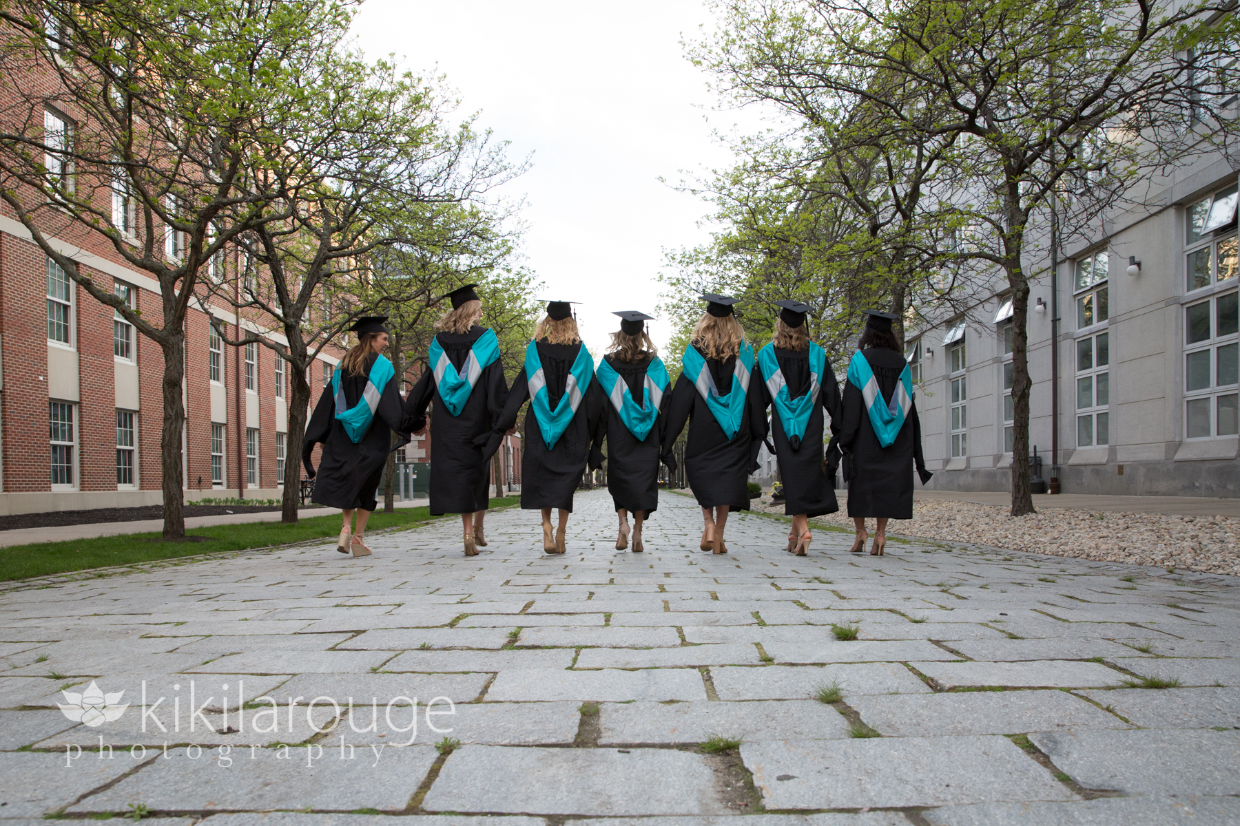 Seven grads in cap and gown walking on cobblestone street