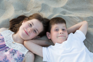 Girl and boy laying in sand smiling