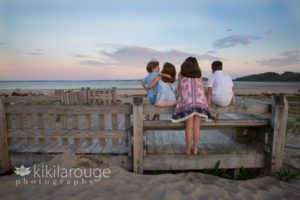 Four kids at sunset beach on boardwalk looking at ocean