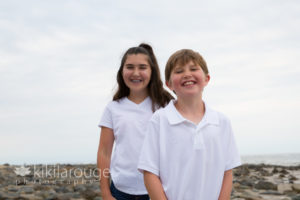 Young girl and boy at rocks at beach laughing