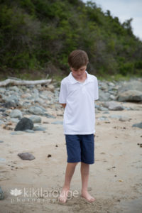 Young boy on beach looking down feet in sand
