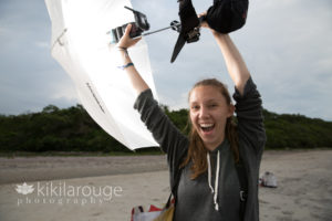Girl grey sweatshirt holding flash and umbrella assisting photo shoot