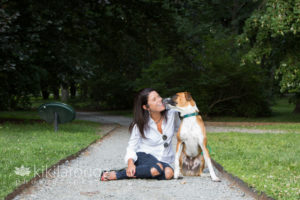 Woman in denim sitting on path with tan dog giving her kisses