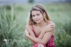 High School girl in red strapless dress sitting in beach dunes