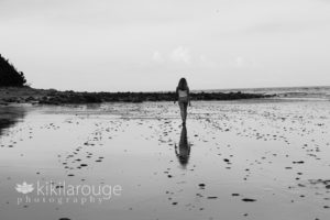 Girl walking away on beach wit reflection in sand
