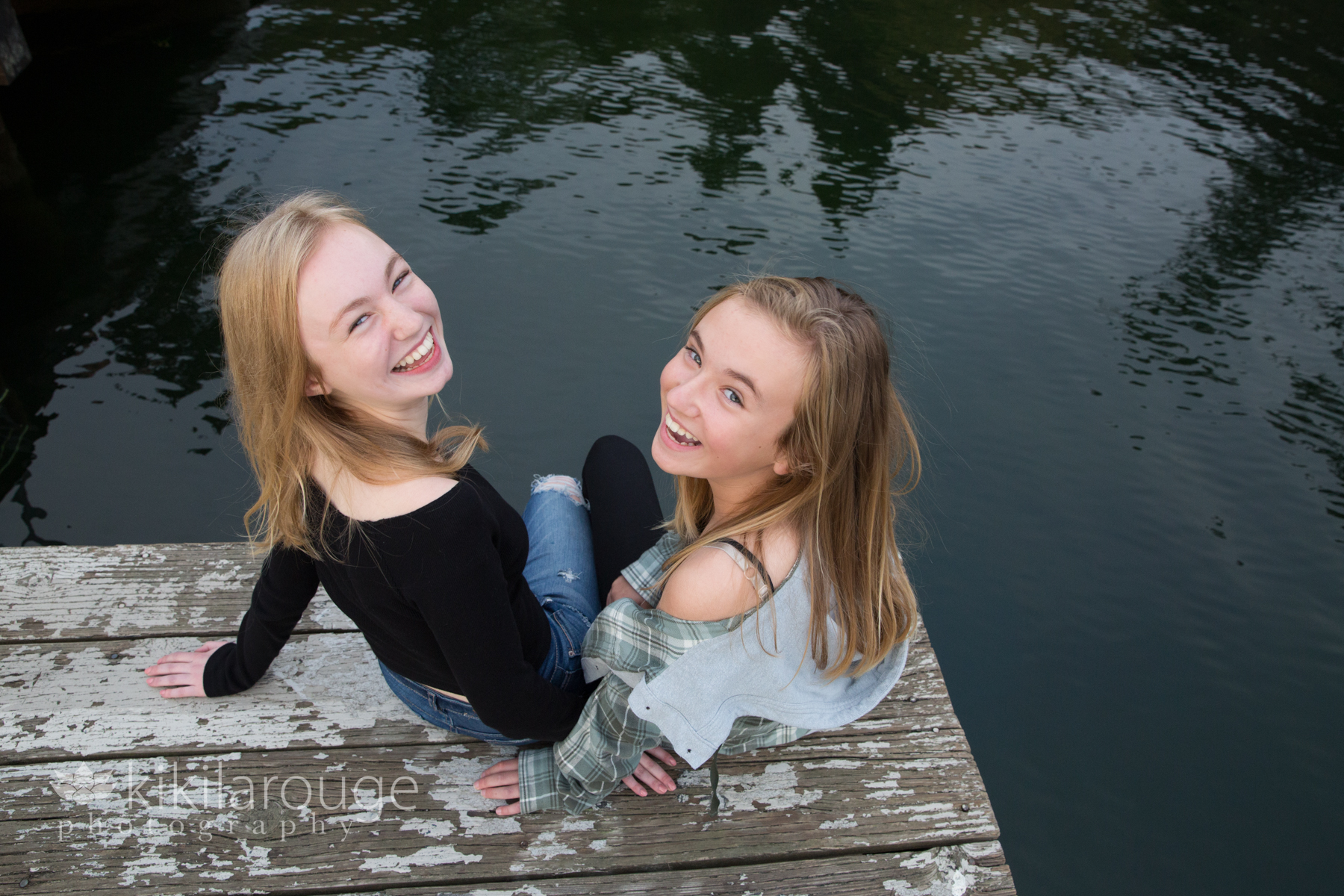 Two girls sitting on dock around water looking up