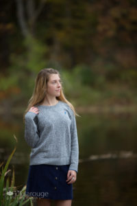 Girl in grey sweater on rock in lake