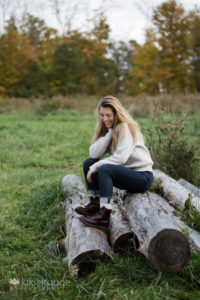 Girl in jeans sitting on logs in field
