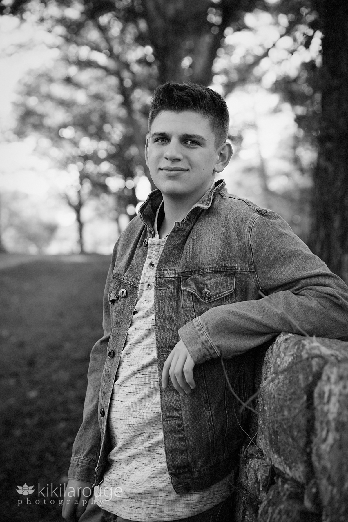 senior Portrait boy in denim jacket leaning on stone wall