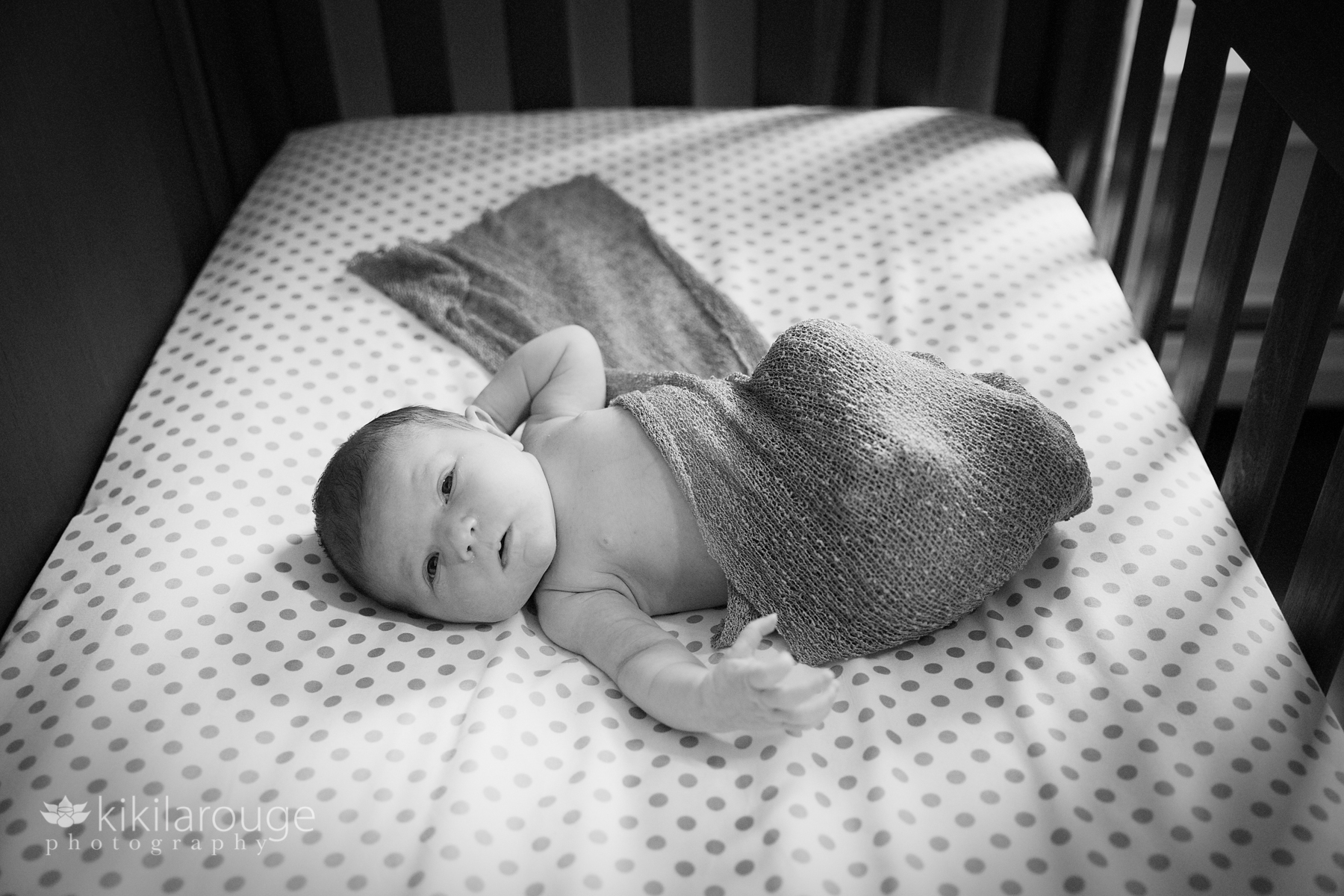 Newborn baby wrapped in swaddle in crib with polka dot sheets