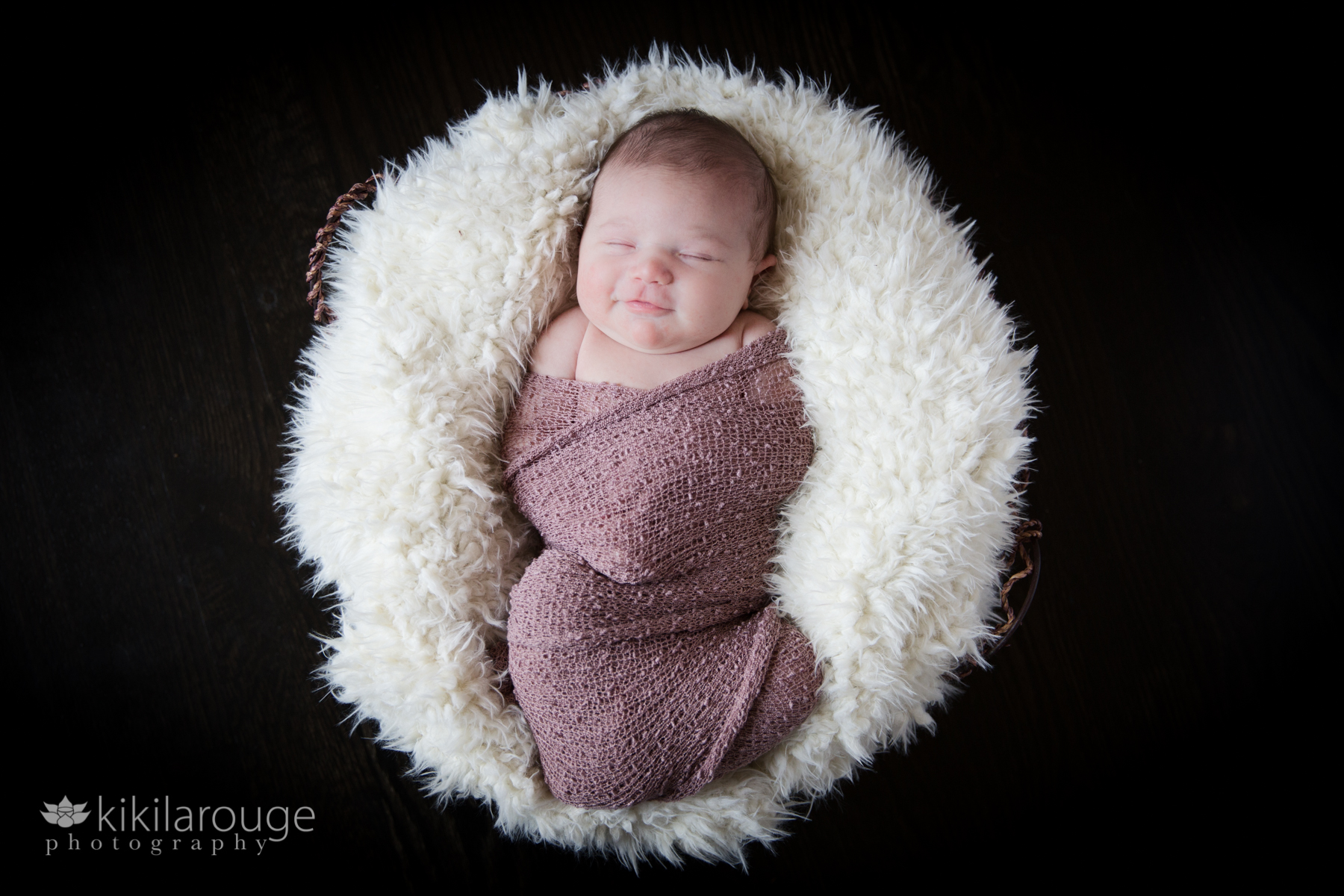 Newborn in basket wrapped in mauve cloth