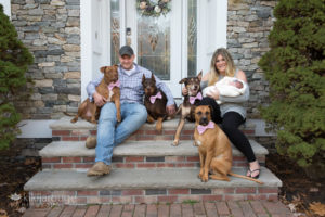 Family with four dogs and newborn on front steps of home