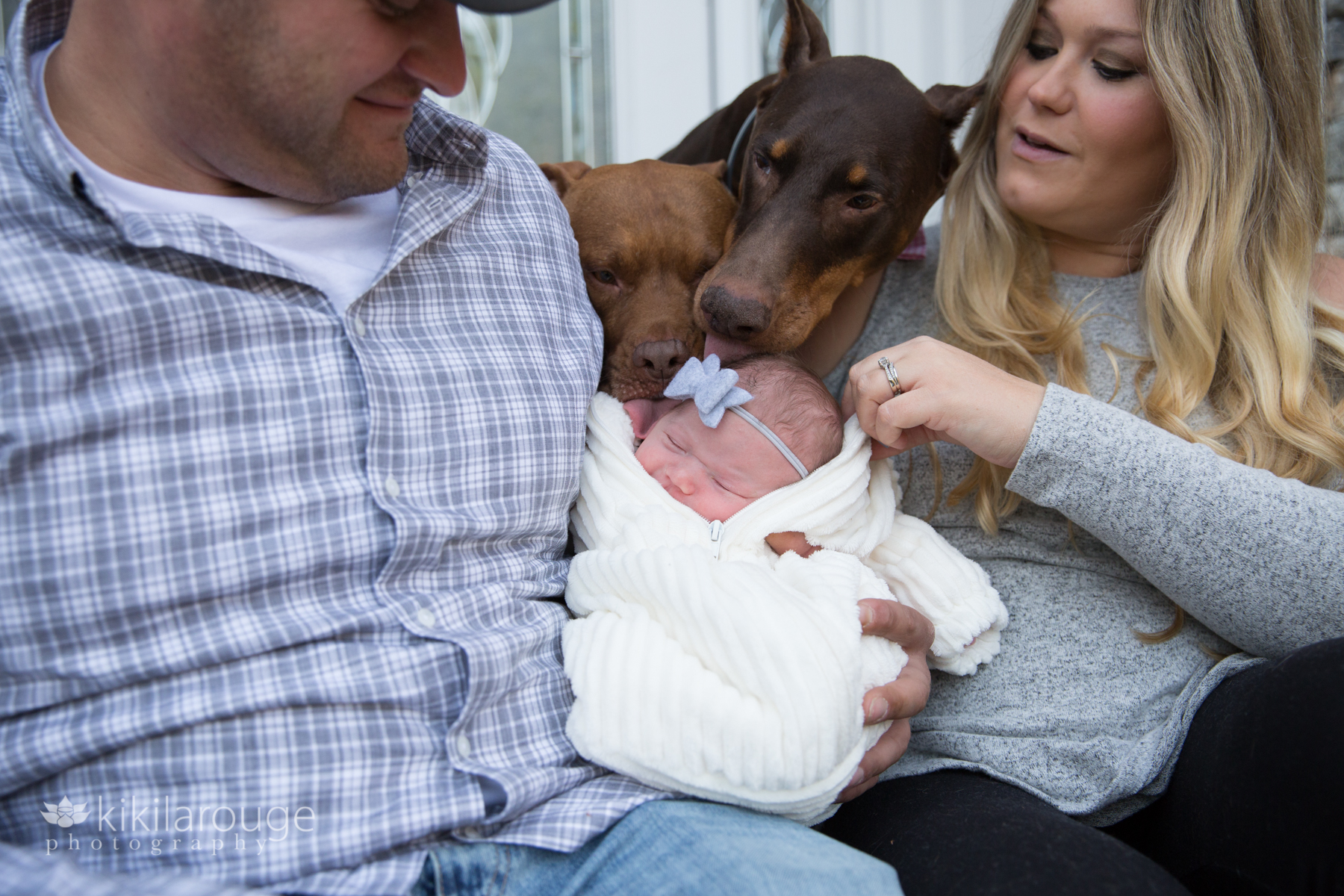 Two dogs kissing newborn baby in dad's arms