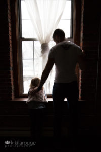 Father and young daughter looking out brick window silhouette