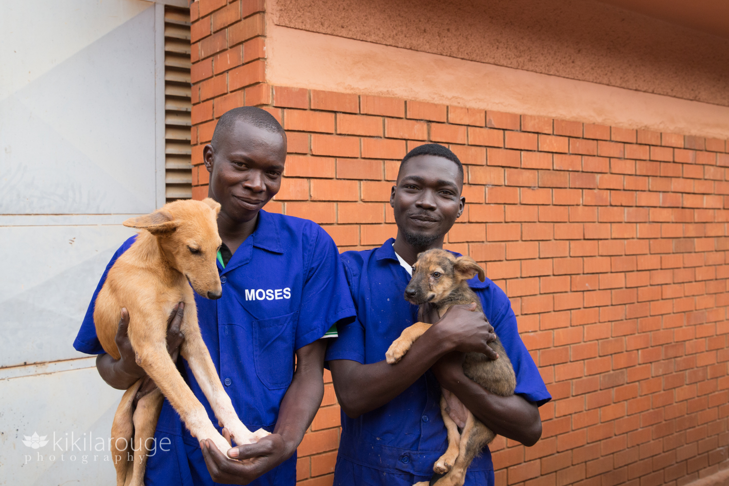 Two men holding rescue dogs at Uganda Animal Shelter