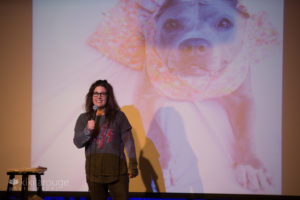 Stand up comedian on stage with projected photo of grey dog behind