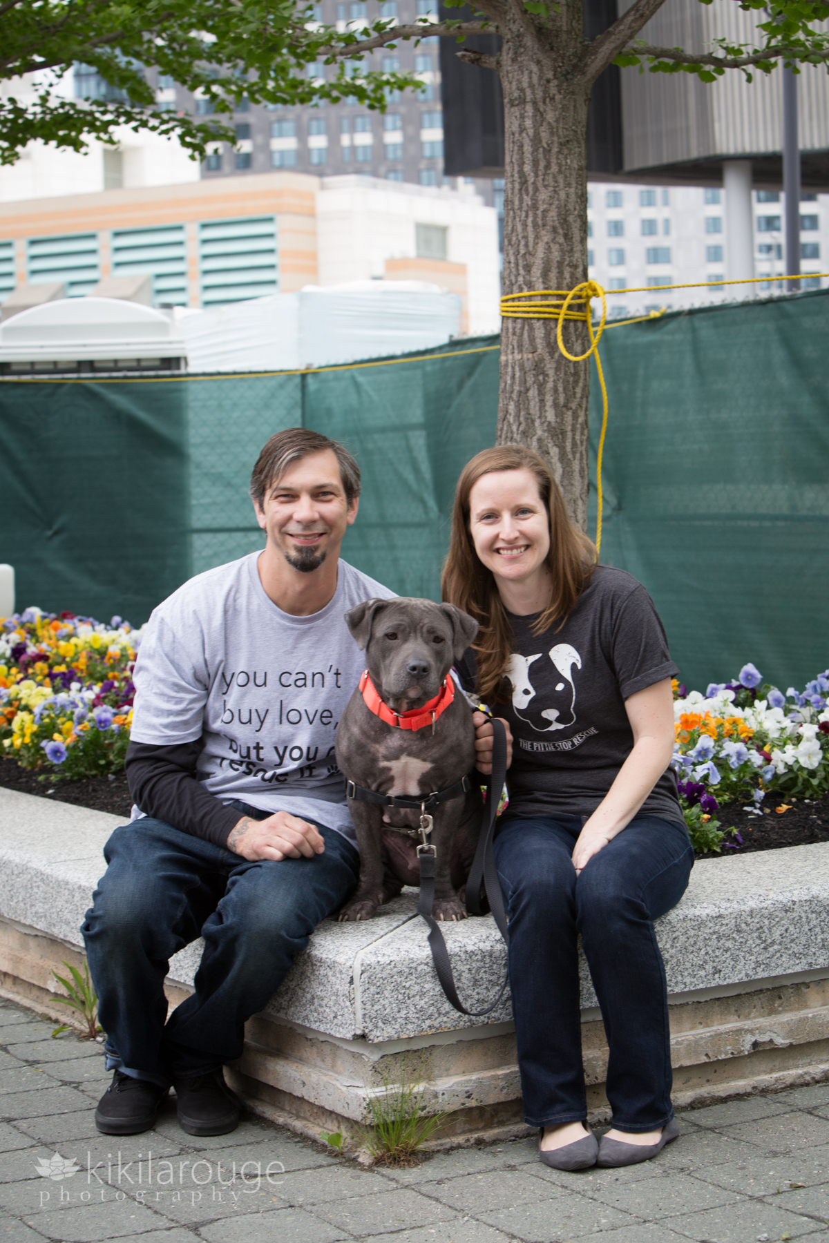 Gray rescue dog sitting by flowers with foster parents