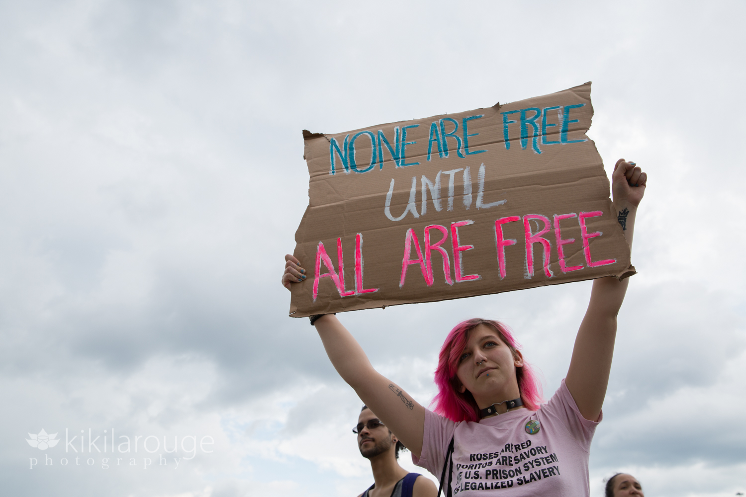 Woman with pink hair and shirt holding ICE protest sign