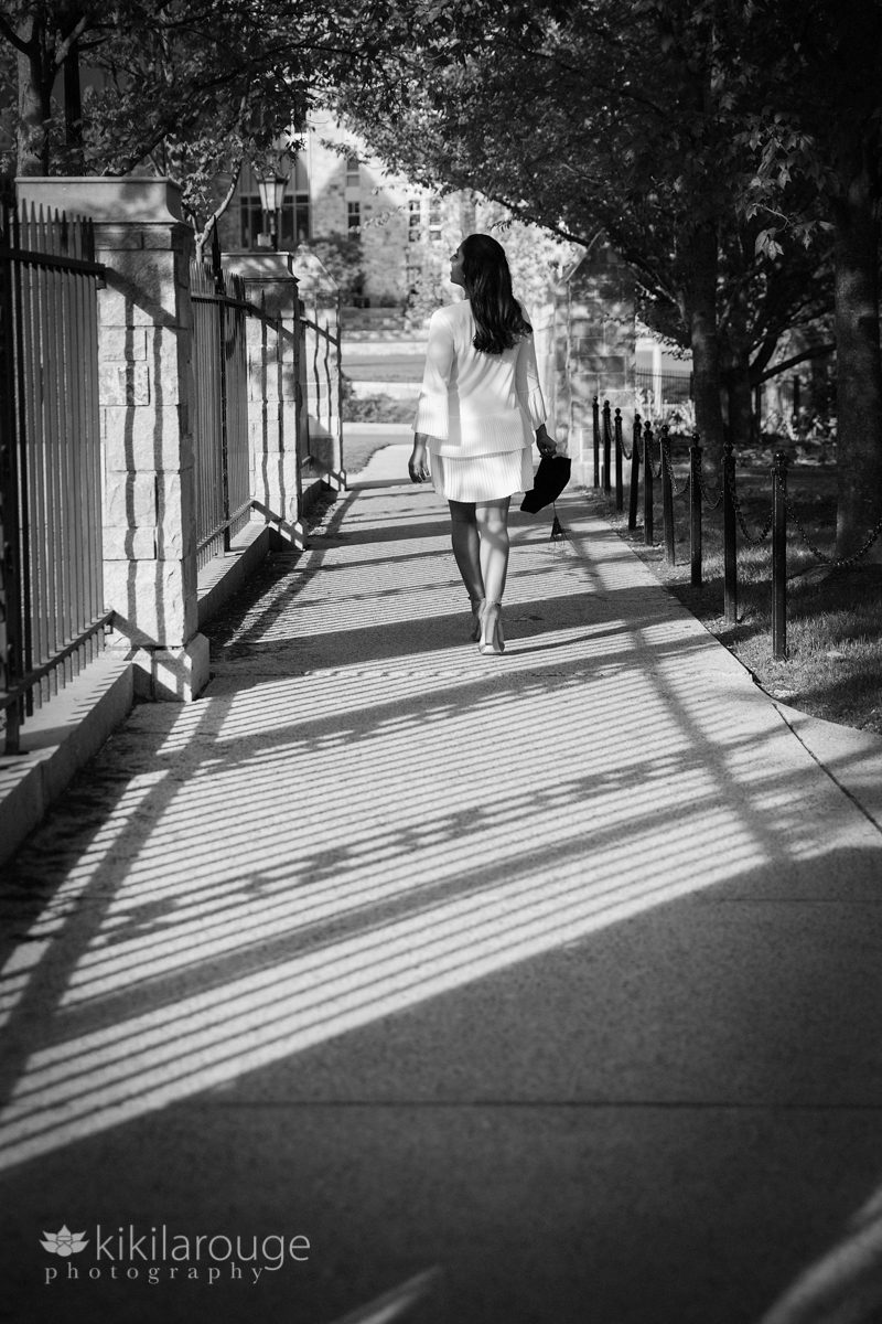Girl in white dress walking away on sidewalk with fence shadows