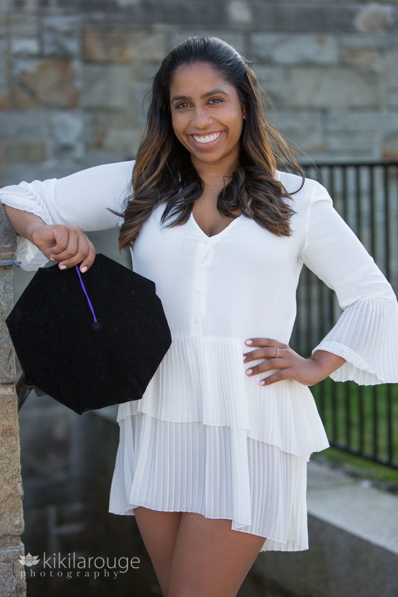 Woman holding graduation cap with purple tassel and white dres
