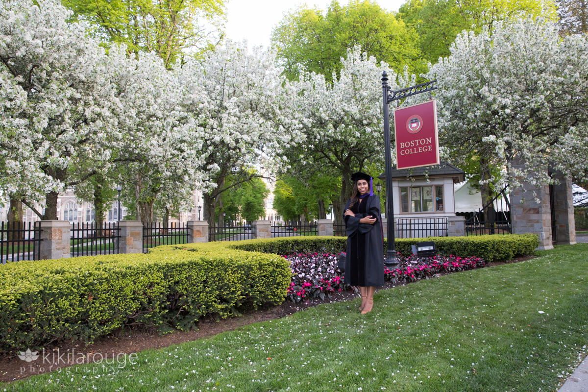 Boston College Graduate laughing front of campus sign with flowers in bloom
