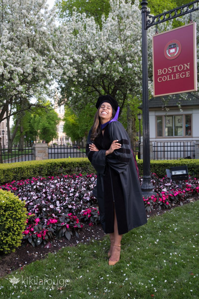 Boston College Graduate in front of campus sign with flowers in bloom