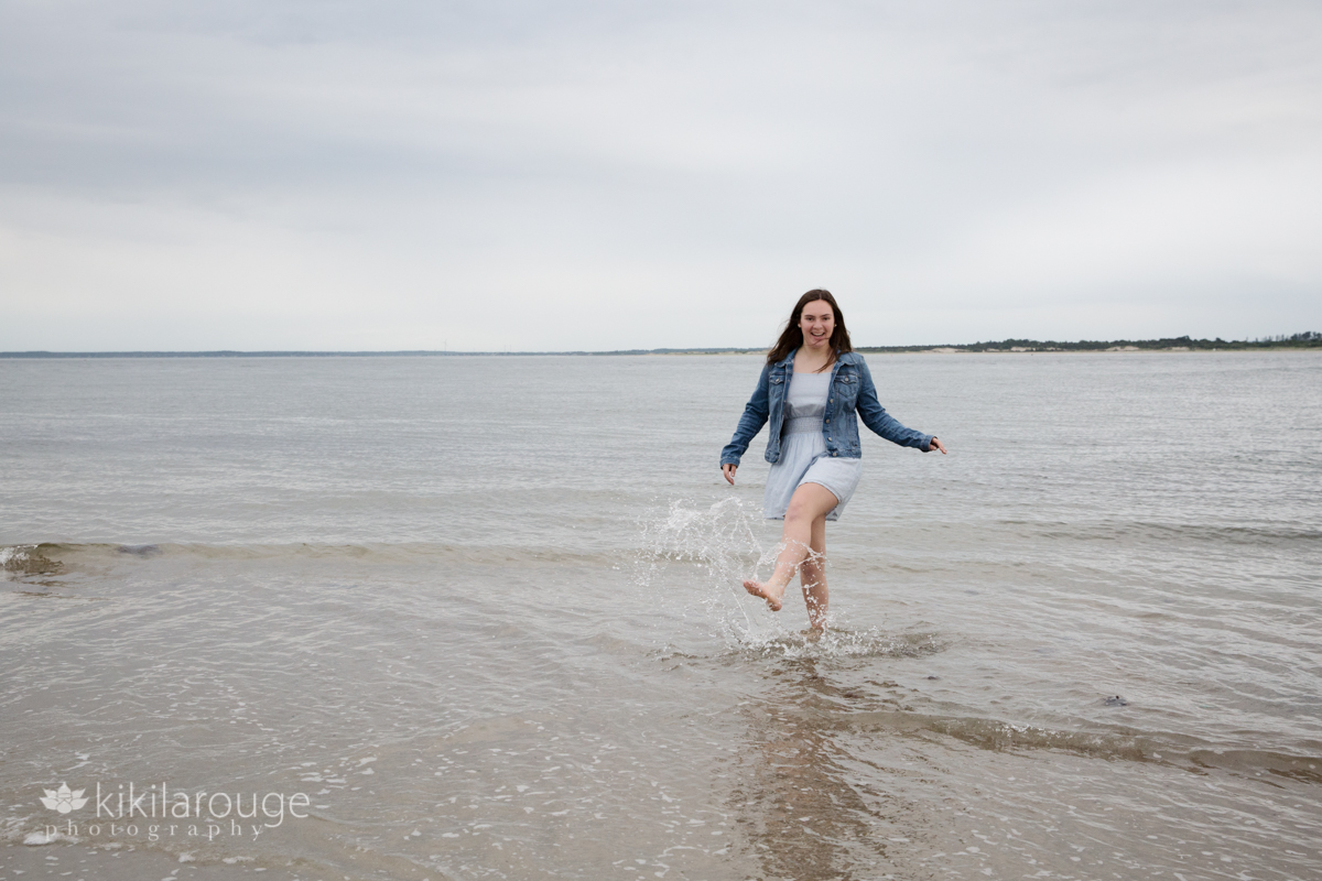 Girl in blue dress kicking water at beach shoreline
