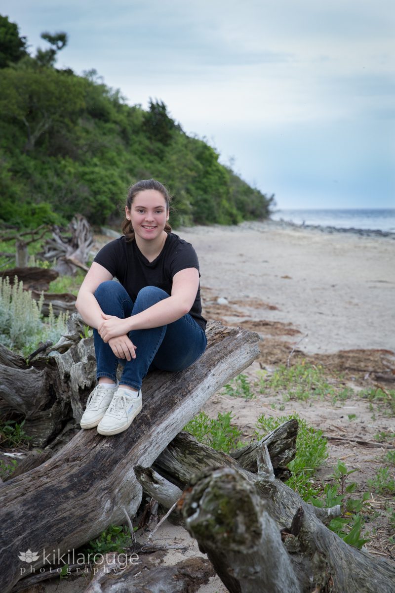 Girl smiling sitting on log at beach