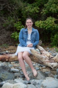 Girl sitting on driftwood in light blue dress and denim jacket