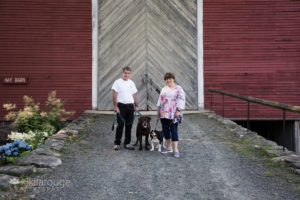 Couple with two dogs in front of gray and red barn