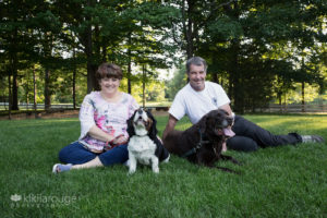 Couple with to dogs sitting in grass at sunset