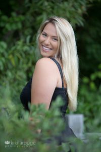 Girl in black denim dress in bushes smiling