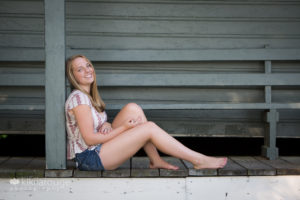 Senior girl in denim leaning on pole on porch