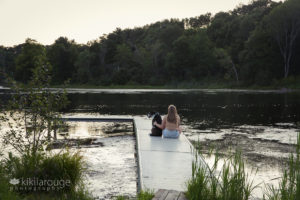 Girl sitting on dock at pond with dog