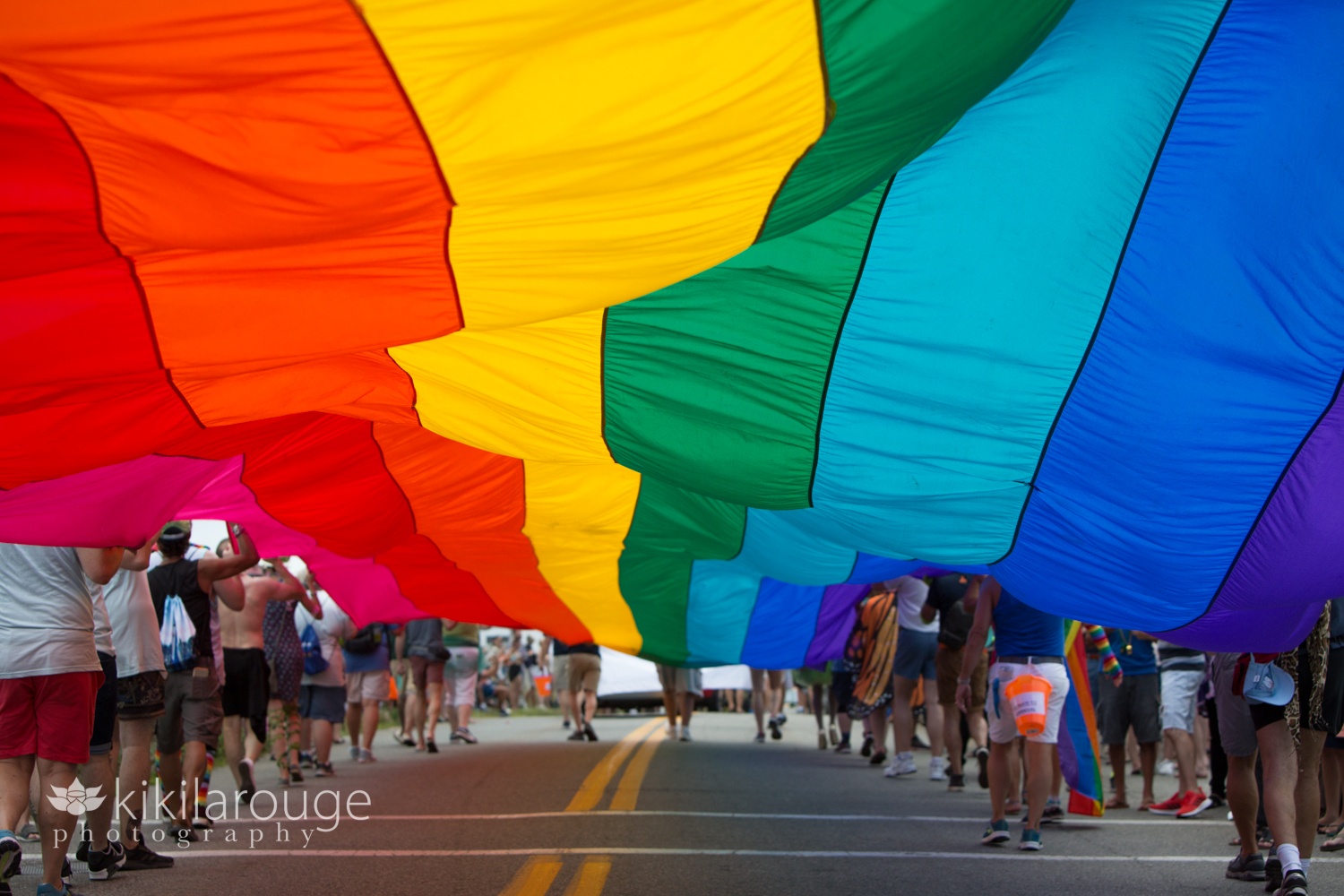 Under large rainbow flag held by many people in parade