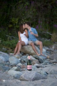 Rose champagne on rock with couple kissing in background