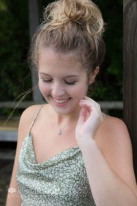 Girl in green tank top with hand near face smiling looking down