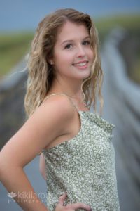 Girl with curly blonde hair leaning on beach boardwalk