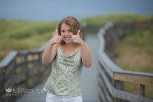 Teen senior girl giving two thumbs up on boardwalk at beach