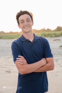 Teen boy in blue polo shirt smiling at sunset beach