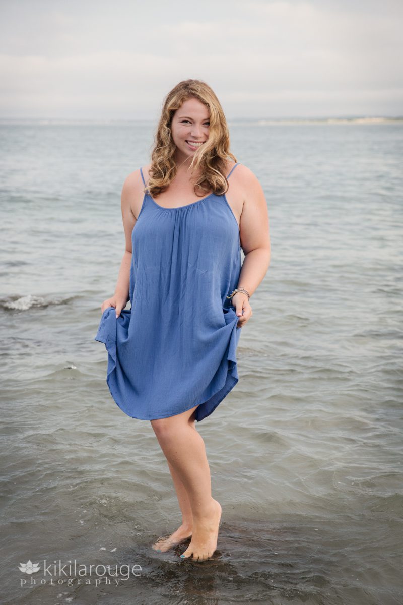 Blonde girl in blue dress standing on rock in ocean