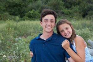 Young girl leaning and hugging older brother by dunes