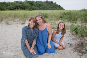 Mom and two daughters leaning in sand at beach laughing