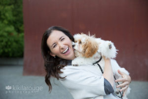 Woman smiling and holding small dog that is kissing her face